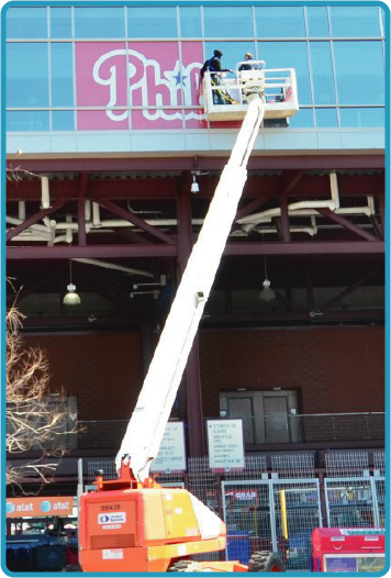 Workers installing a Philadelphia Phillies logo on an office window using a boom lift.